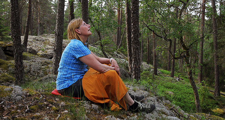 En kvinna sitter på marken i en skog.