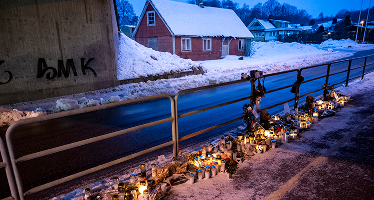 Ljus och annat ligger på marken intill en å. Det är snö på marken och på taken på husen.