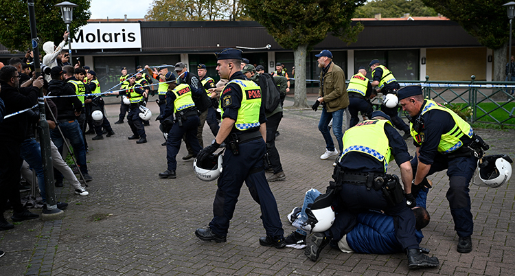 Flera poliser sitter på en person. Andra poliser står framför demonstranter.