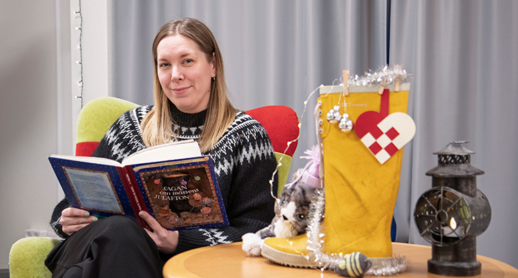 Hon sitter i en fåtölj och läser ur en bok.