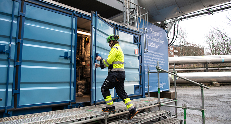 En man i gul overall är på väg in i en blå container med rör i.