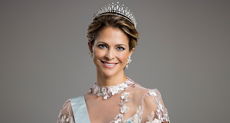 Hon är uppklädd med tiara och festklänning och ler in i kameran.