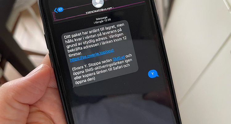 En hand håller en mobil med ett falskt sms som någon svarat på.