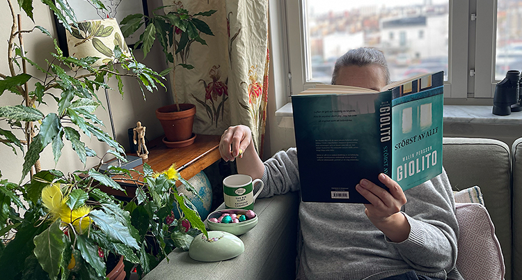 En person sitter i en soffa och läser en bok. Vid sidan av soffan står ett påskägg med godis.