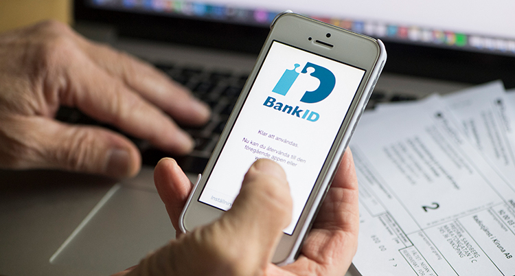 En äldre man håller i en mobil med bank-id. Bara mannens händer syns.