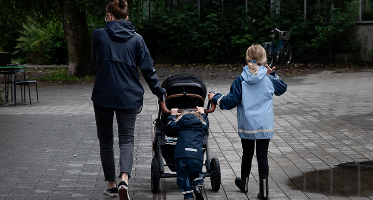 En mamma med två små barn som drar en barnvagn.