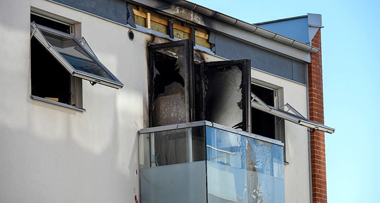 En balkong i ett hus med lägenheter. Dörren och rummet bakom balkongen är utbränd.