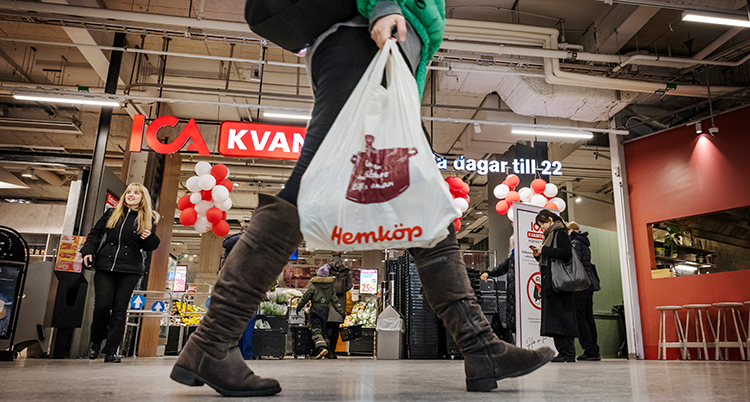 En person går med en kasse med mat framför ingången till en affär för mat.