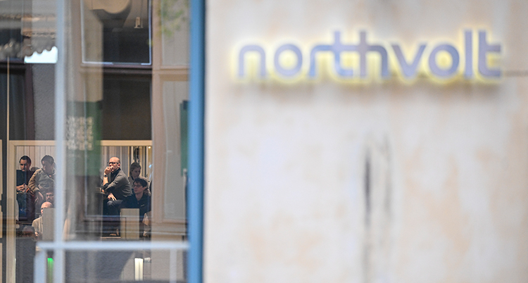 En skylt som det står Northvolt på. Det går att se folk genom ett fönster.