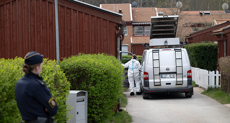 En polis står vid en häck. En annan person jobbar vid en skåpbil.
