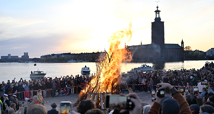 Många människor står runt en eld. Det är vatten bakom. Stadshuset syns på andra sidan.