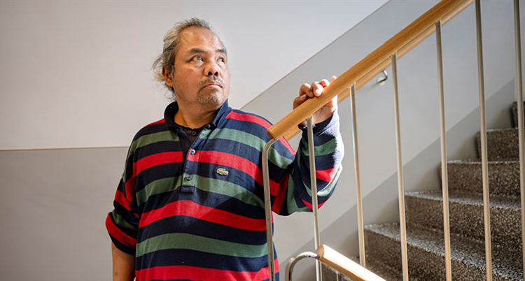 Han står i ett trapphus. Han håller i trappräcket.