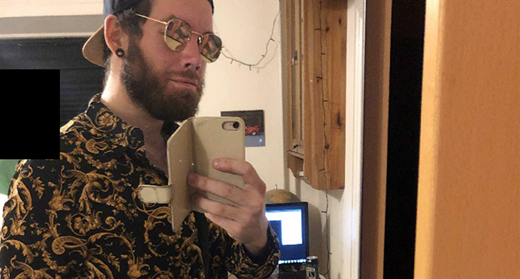 Han tar en bild på sig själv med sin mobil. Han har keps och solglasögon.