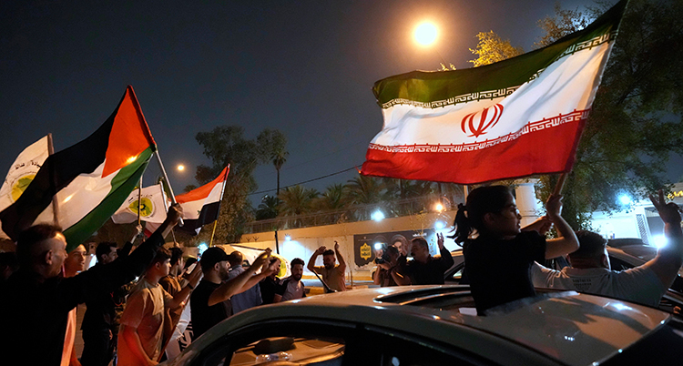De står vid sina bilar och viftar Irans flaggor.