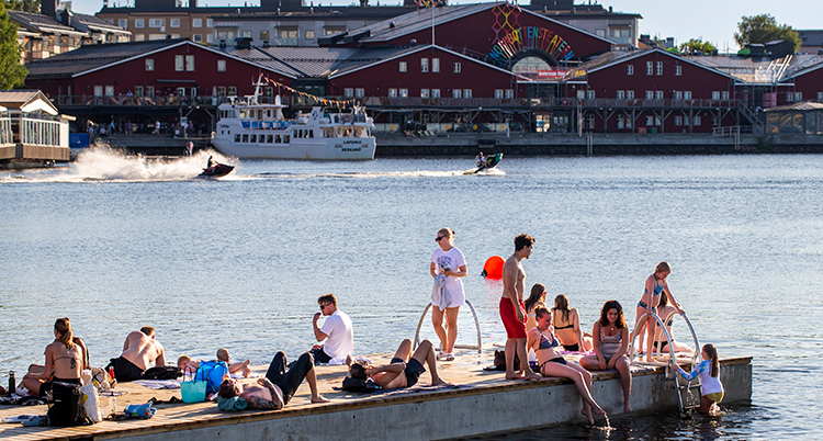 Flera personer sitter på en brygga i vattnet.