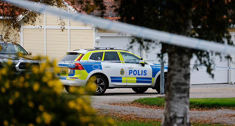 En polisbil står parkerad vid ett garage. Poliserna har spärrat av med band.