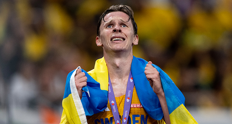 Han har en svensk flagga över axlarna. Han ser ledsen och glad ut.