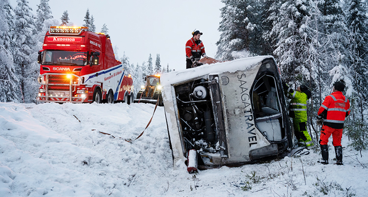 Det är snö ute. En buss ligger i diket. Folk är där och jobbar.