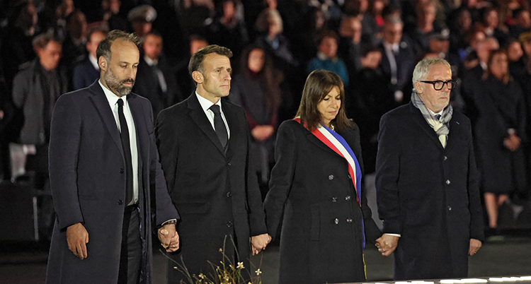 Macron och tre andra personer håller varandra i hand under en ceremoni.