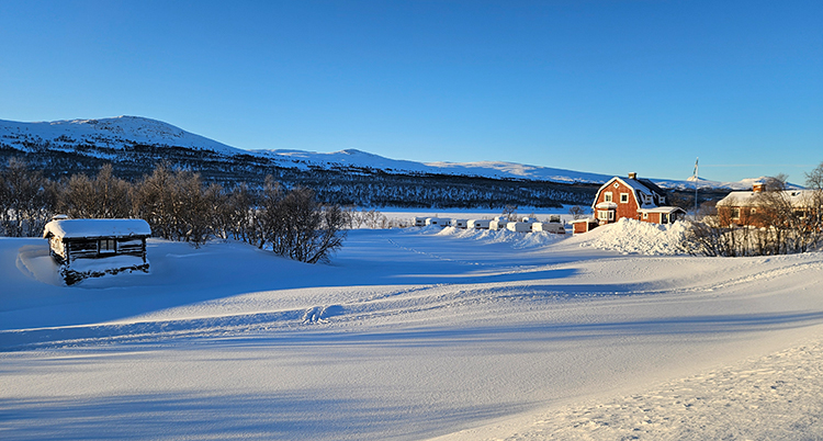 En snöig dal i fjällen. Himlen är blå.