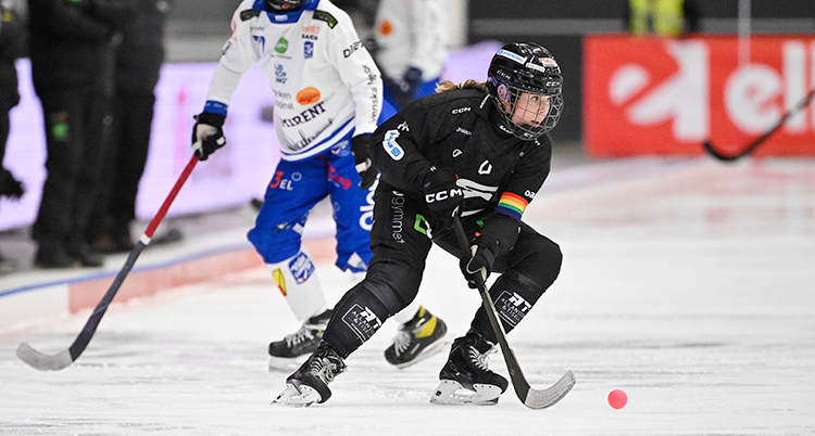 En match i bandy. En spelare i svarta kläder har bollen.