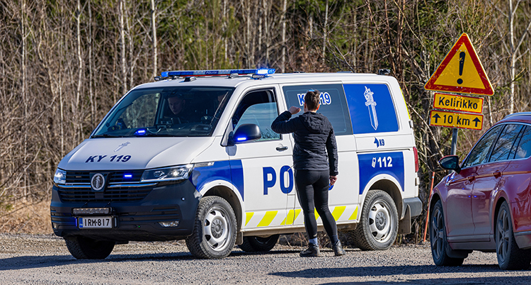 En polisbuss står på en väg. Ee kvinna pratar med en polis i bilen.