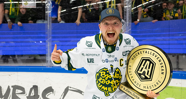 Han har hockeytröja och hjälm och håller i ett pris. Han jublar.