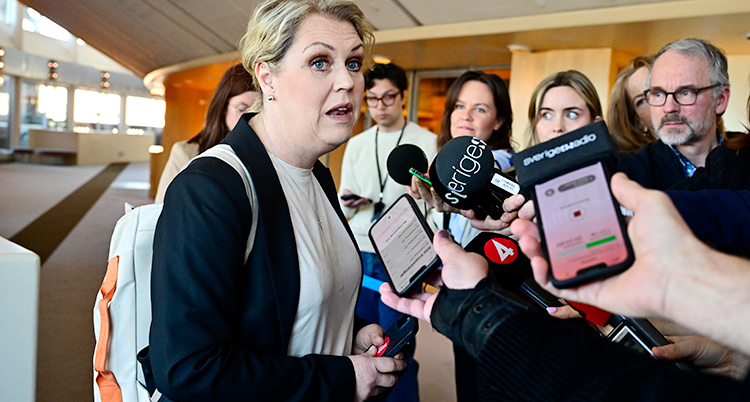 Hon står i riksdagen och blir intervjuad av flera journalister.