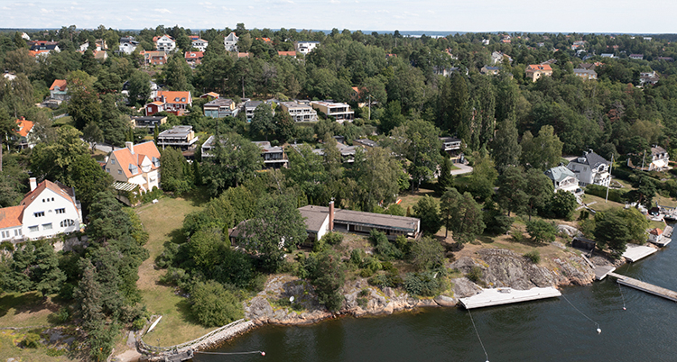 Bild tagen från luften. Hus, grönska och bryggor i vatten syns.