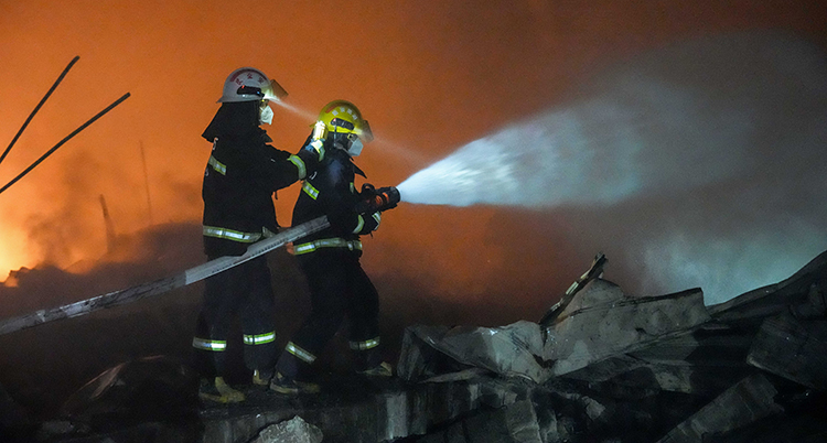 Två brandmän sprutar vatten. Det är mörkt. I bakgrunden syns elden.
