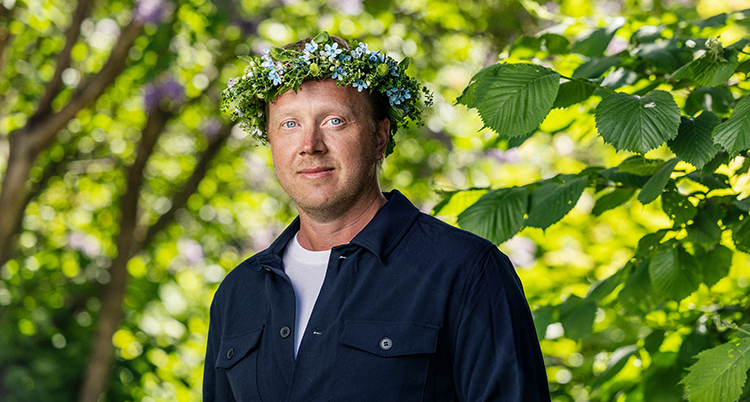 Han tittar in i kameran. Han har en blomsterkrans på huvudet.
