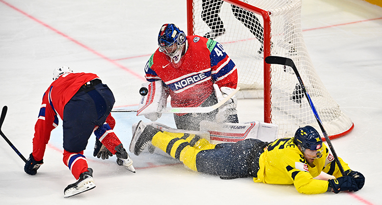 En svensk spelare ligger framför det norska målet. Målvakten står i målet.