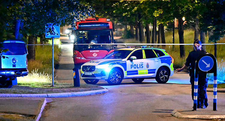 En polisbil och en buss står parkerade. Det är mörkt. En polis står vid sidan om.