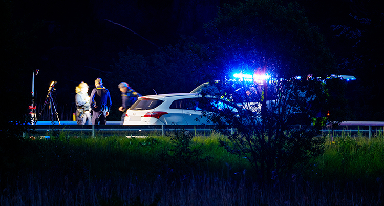 Det är mörkt. Flera poliser står vid en vit bil.