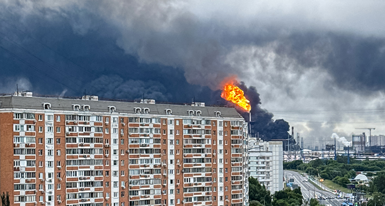 Eld och rök stiger mot himlen bakom ett stort hus för lägenheter.