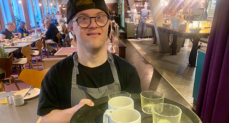 Han bär en bricka med muggar och glas.