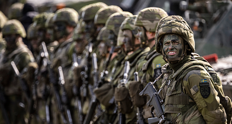 De står på en rad i gröna kläder. En soldat tittar mot fotografen och ler.