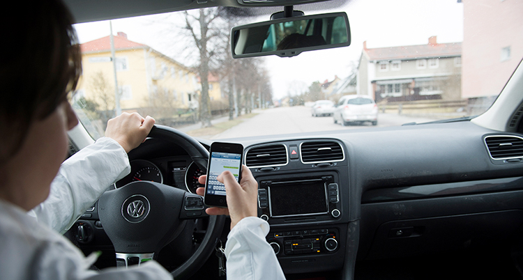 En kvinna håller på med sin mobiltelefon samtidigt som hon kör bil.