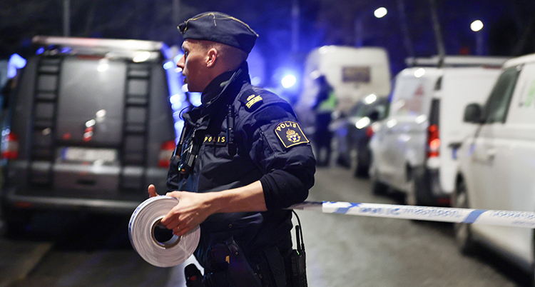 En polis rullar ut band för att stänga ett område. Det är mörkt ute.
