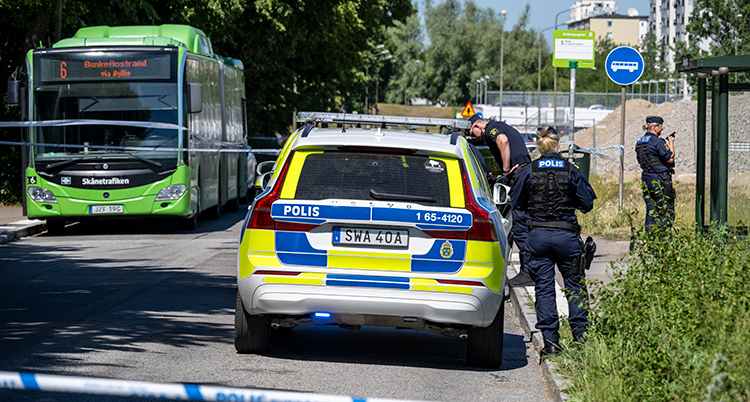 En polisbil har parkerat nära bussen. Flera poliser jobbar vid platsen.