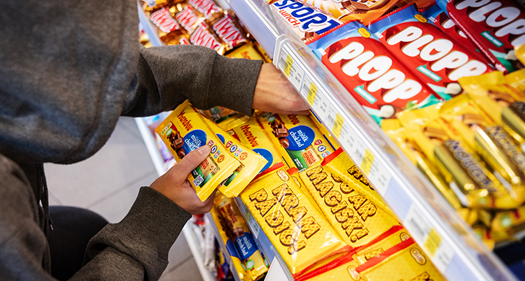 En person med luva för huvudet tar godis i en hylla.