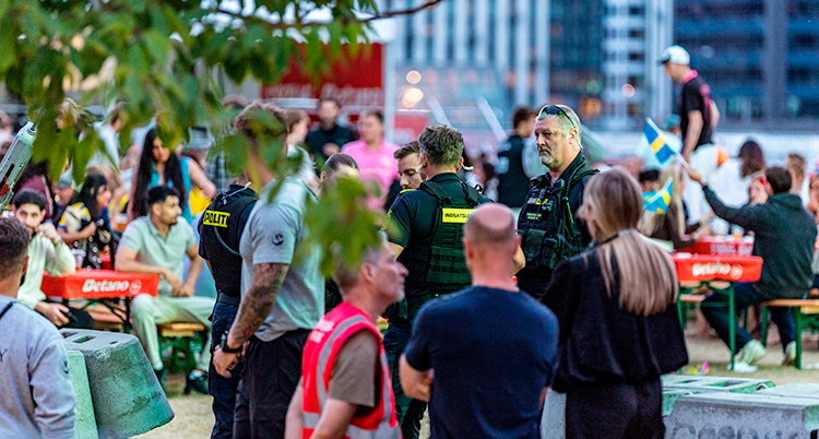 Några poliser står och pratar. Runt om finns folk som samlats för att se fotboll på stor tv.