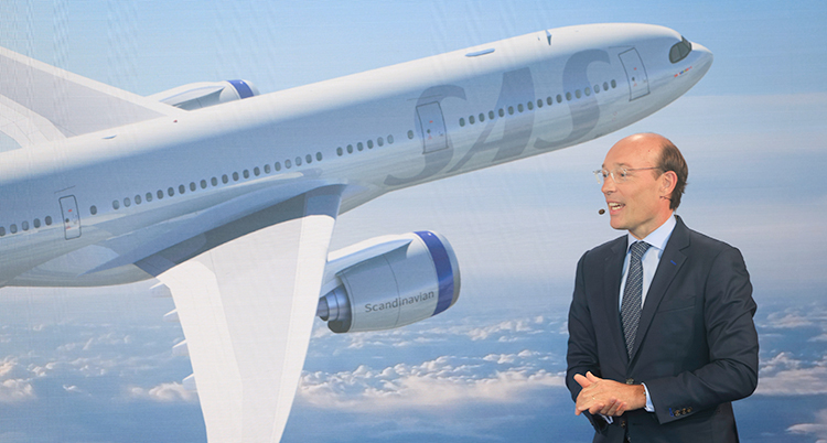 Han står och pratar framför en bild av ett flygplan.