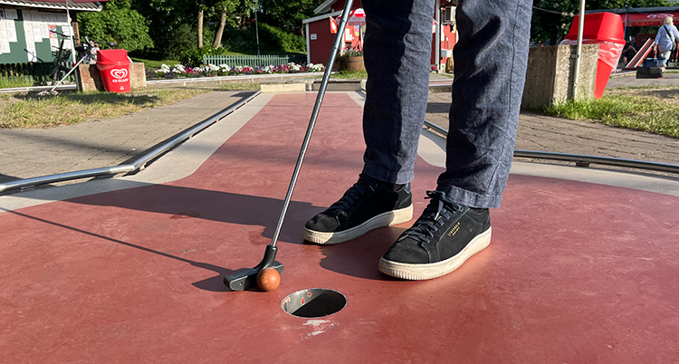 En person står på en bana för minigolf och ska slå bollen i hål.