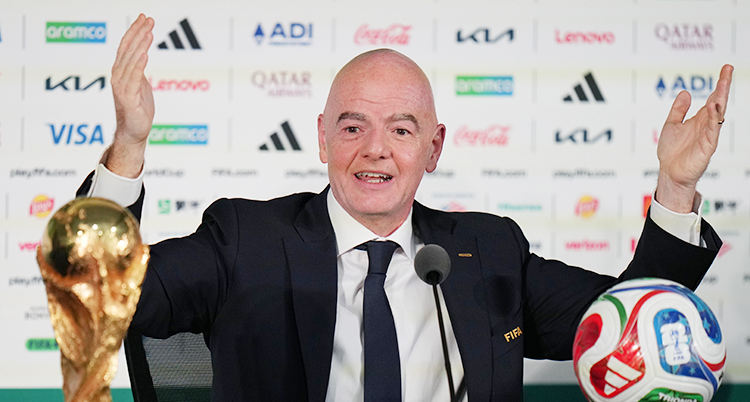 Han är på ett möte med journalister. Han håller upp armarna. Framför sig har han VMs pokal och en fotboll.