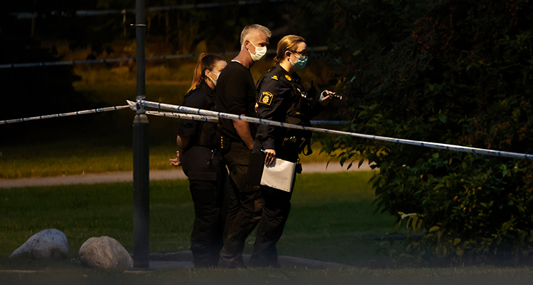 De står vid polisernas band nära en gatlampa i mörkret.